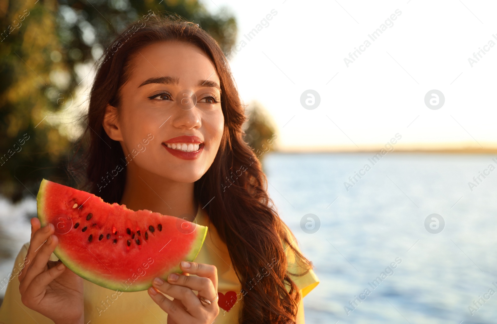 Photo of Beautiful young woman with watermelon near river. Space for text