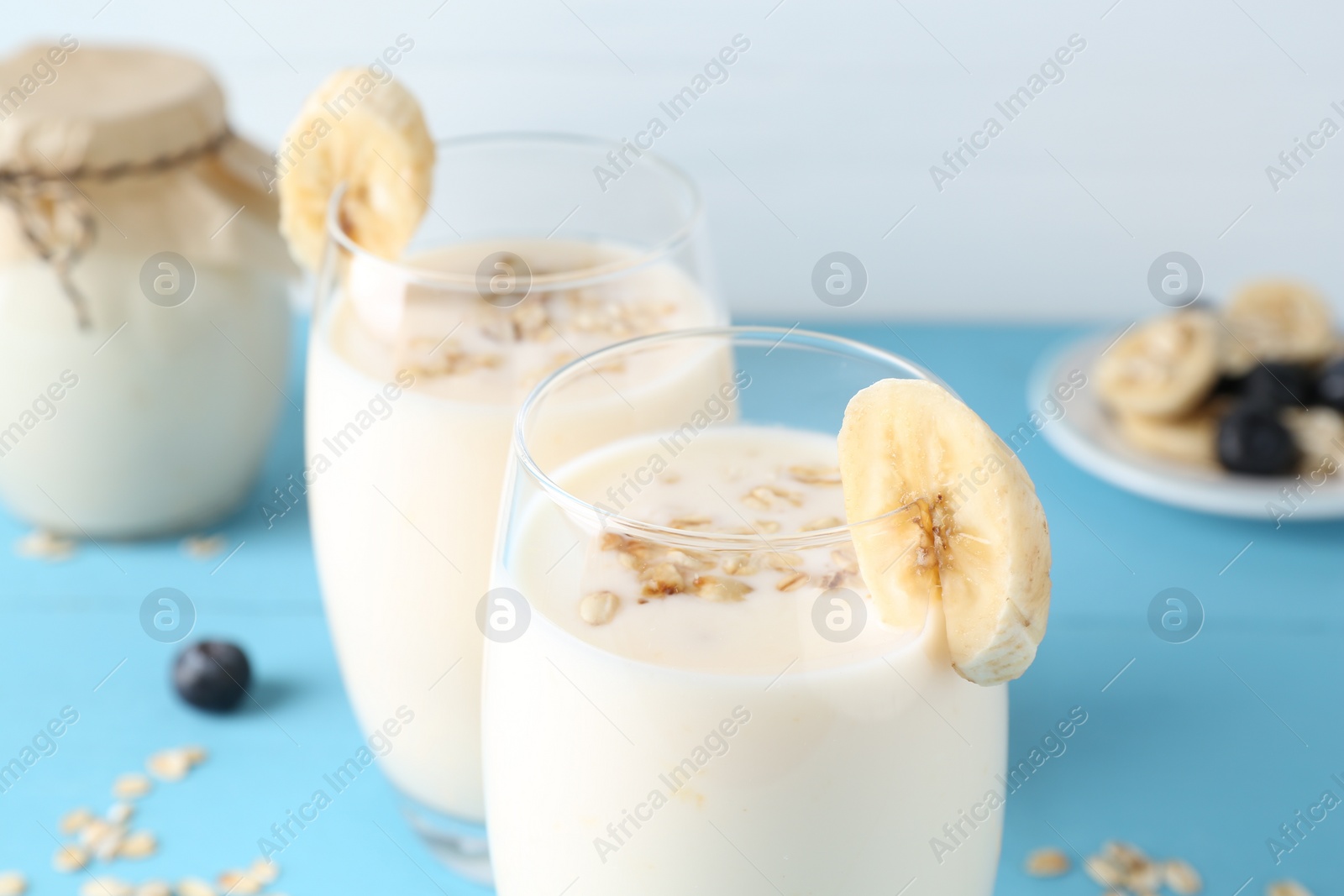 Photo of Tasty yogurt in glasses, oats, banana and blueberries on light blue table, closeup