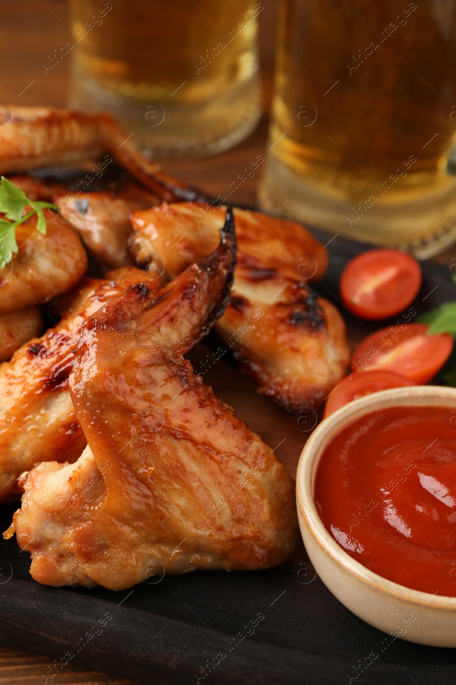 Photo of Delicious baked chicken wings, sauce and mugs with beer on table, closeup
