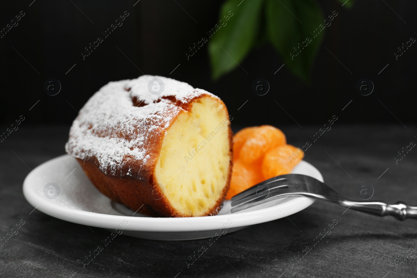 Photo of Piece of delicious homemade yogurt cake with powdered sugar and tangerines on gray table