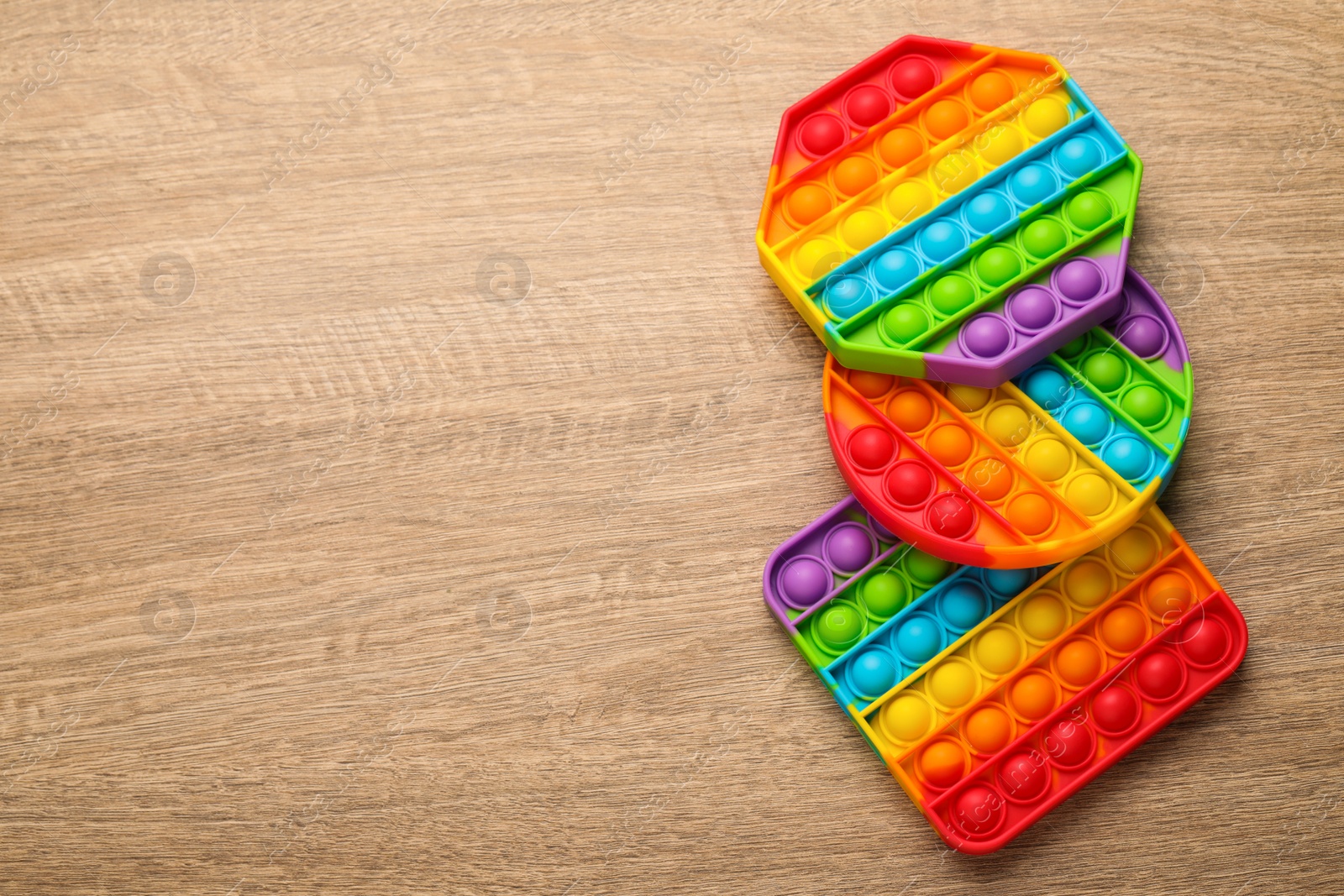 Photo of Rainbow pop it fidget toys on wooden table, flat lay. Space for text