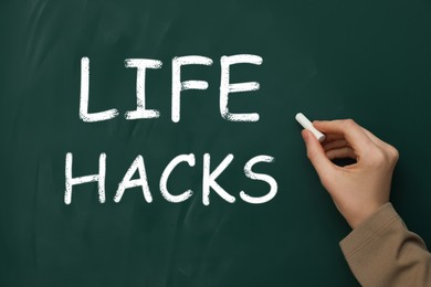 Woman writing words Life Hacks on green chalkboard, closeup