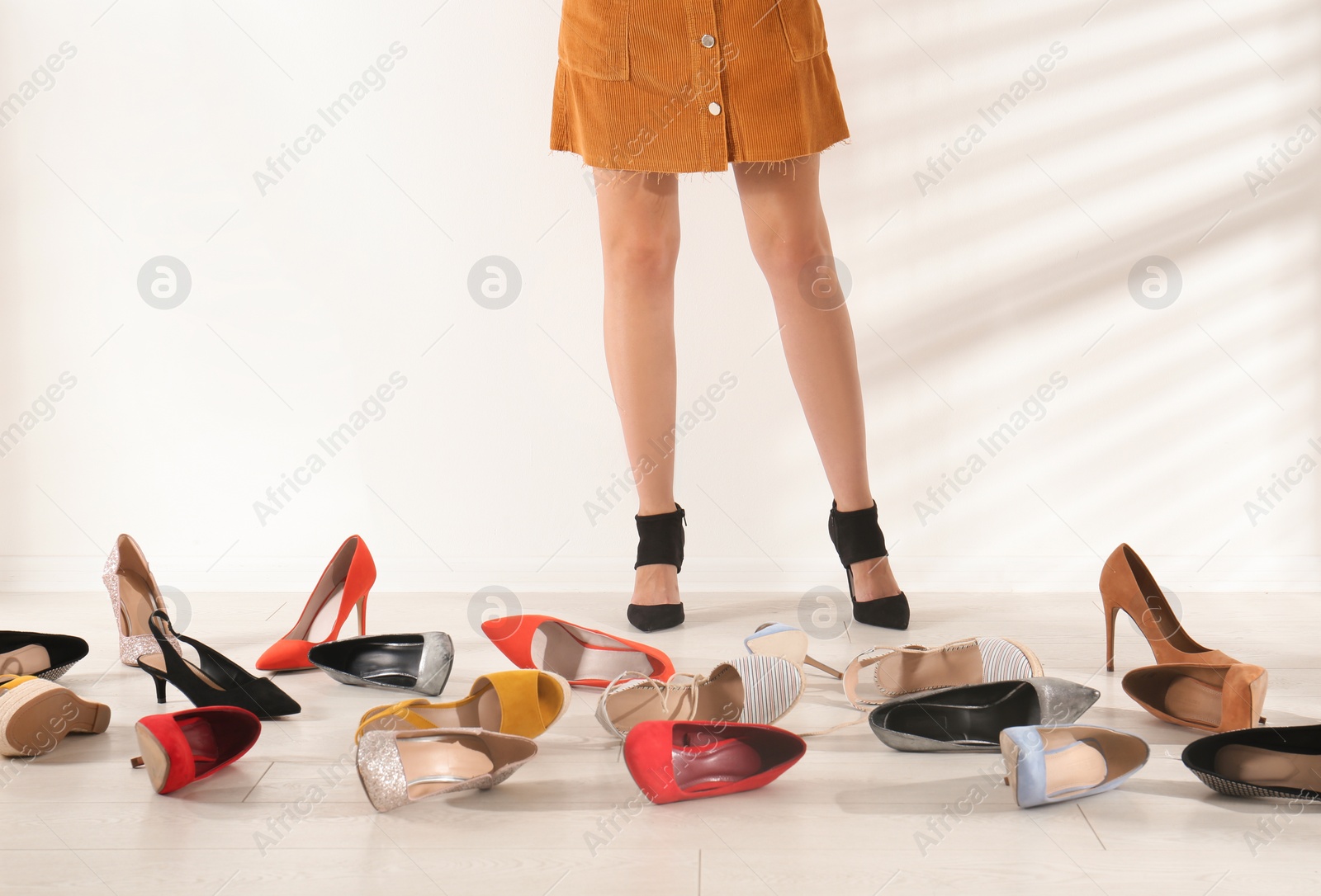 Photo of Woman trying on different high heel shoes near light wall, closeup