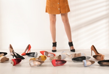 Photo of Woman trying on different high heel shoes near light wall, closeup