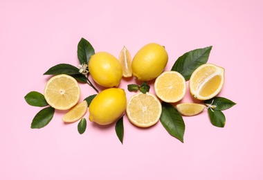 Many fresh ripe lemons with green leaves and flowers on pink background, flat lay