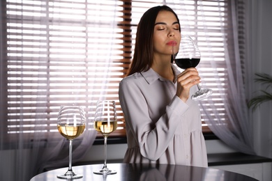 Photo of Beautiful young woman tasting luxury wine at table. Space for text