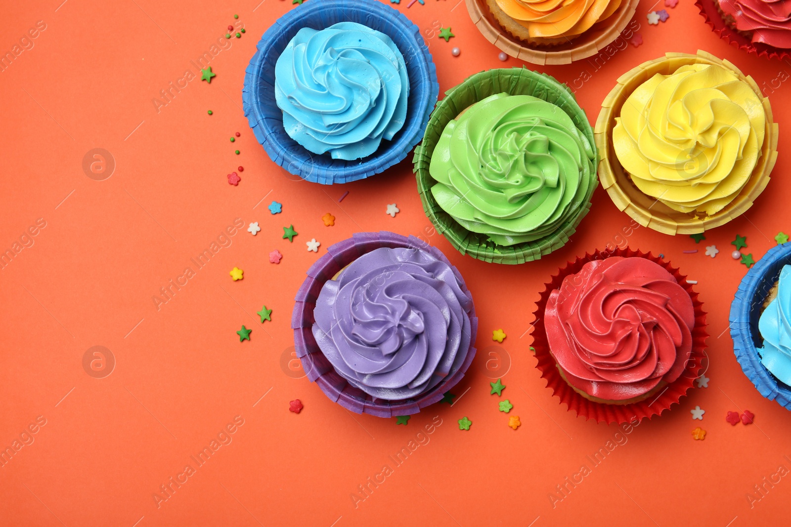 Photo of Delicious bright cupcakes and sprinkles on coral background, flat lay. Space for text