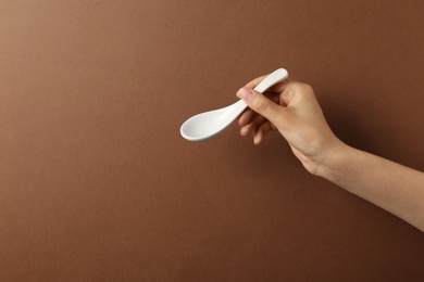 Photo of Woman holding empty miso soup spoon on color background, closeup. Space for text