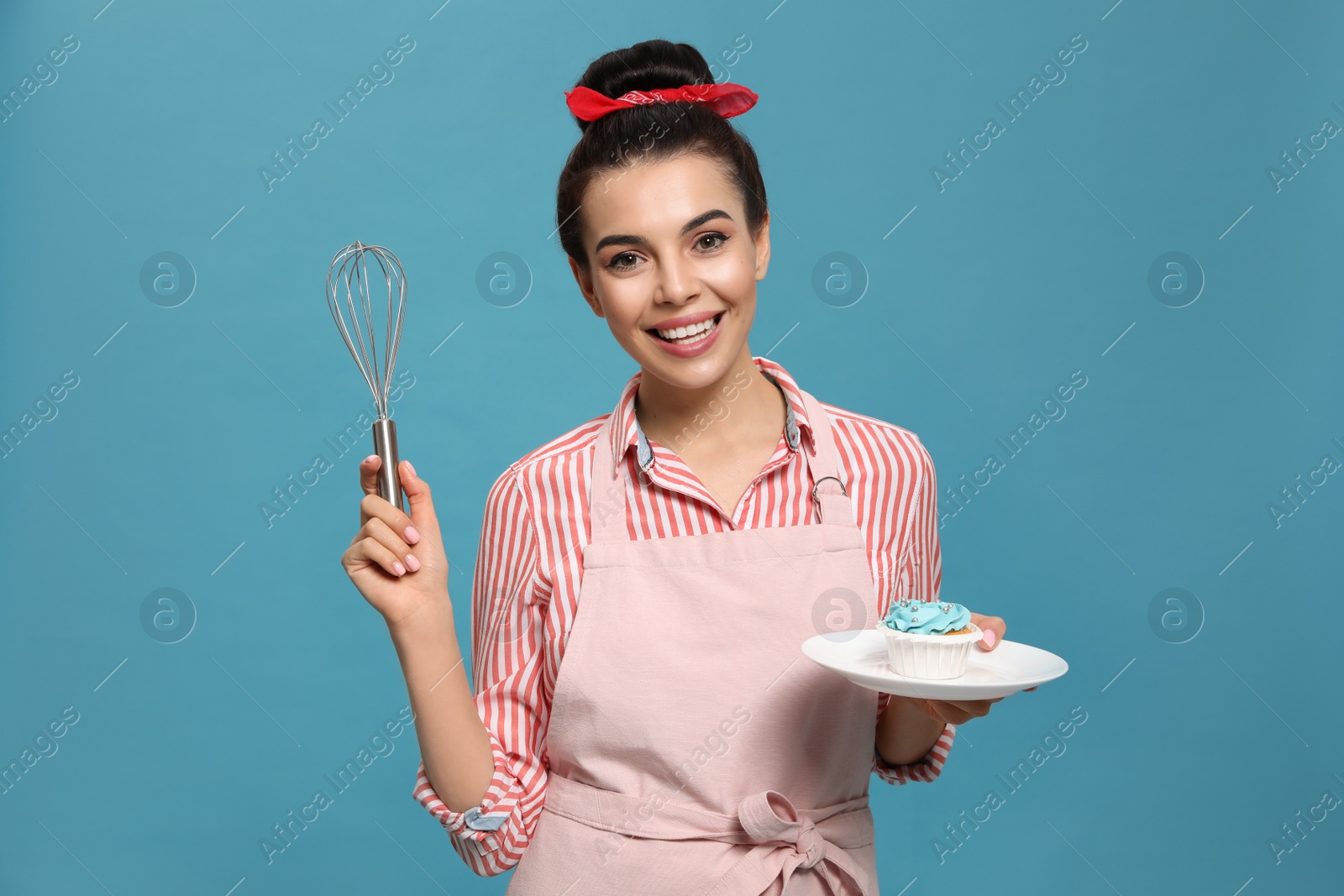 Photo of Young housewife with tasty cupcake and whisk on light blue background
