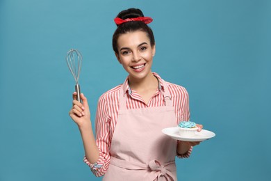 Young housewife with tasty cupcake and whisk on light blue background