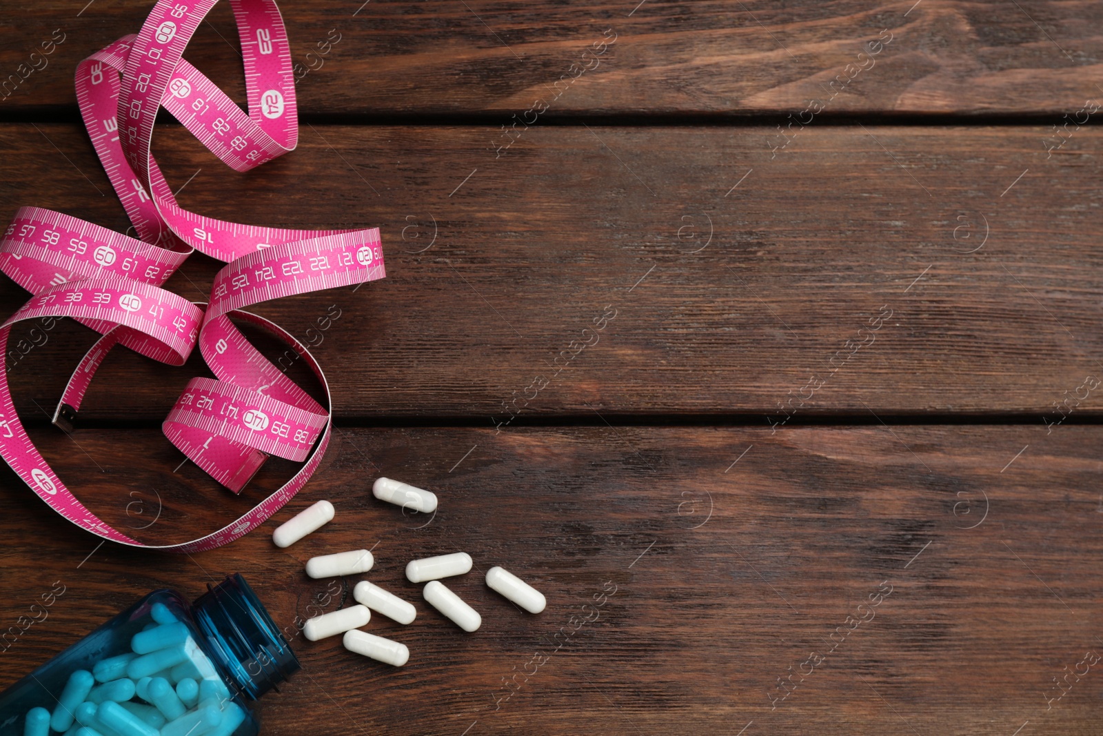 Photo of Jar of weight loss pills and measuring tape on wooden table, flat lay. Space for text