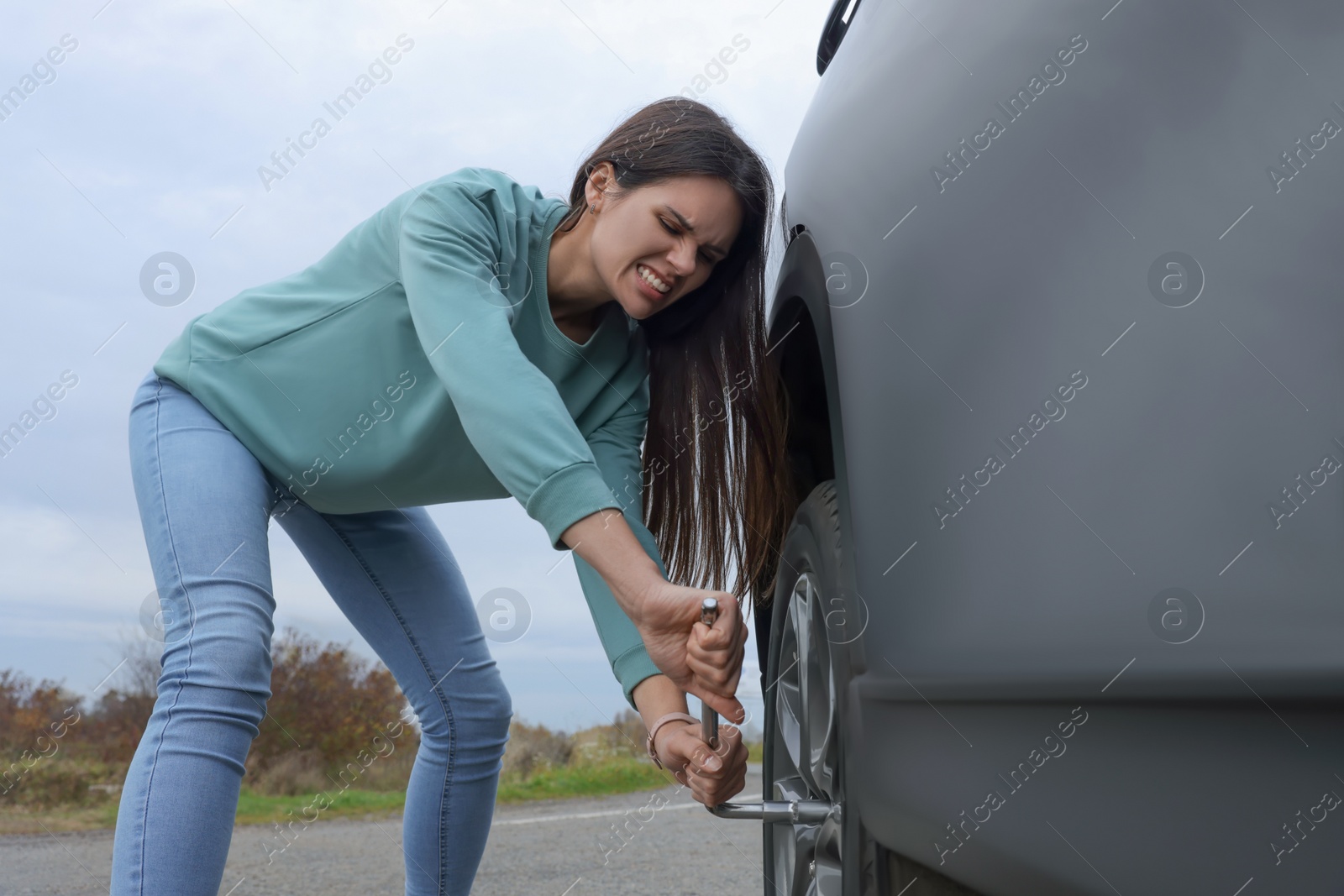 Photo of Young woman changing tire of car outdoors