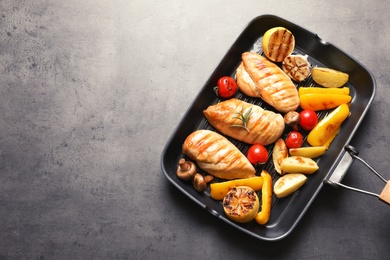 Photo of Grill pan with fried chicken breasts and garnish on grey background, top view. Space for text