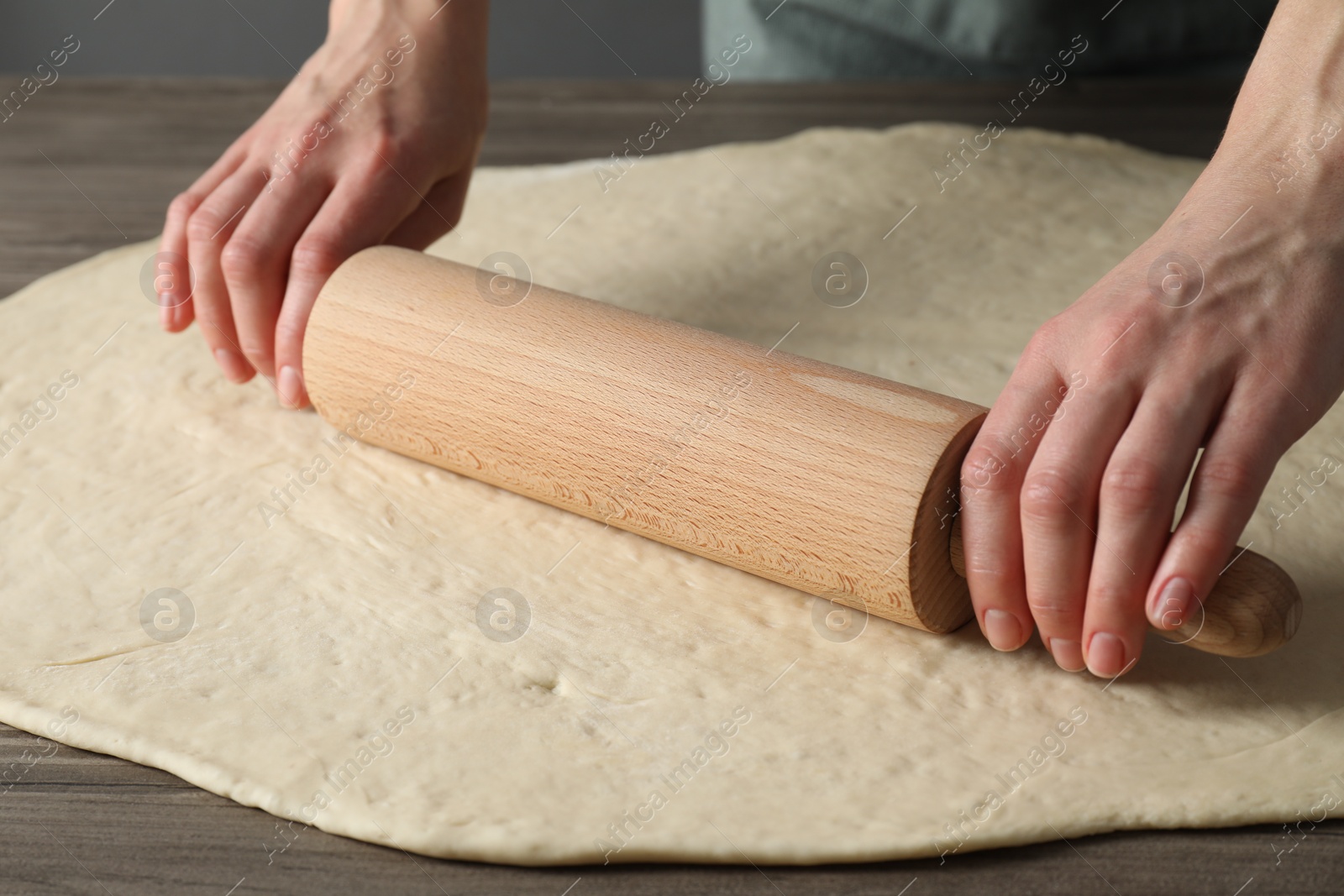 Photo of Woman rolling raw dough at wooden table, closeup