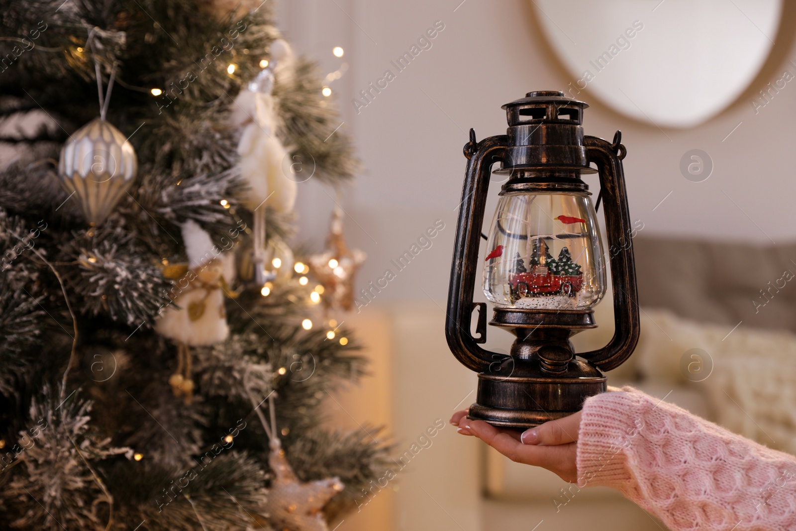 Photo of Woman holding snow globe near Christmas tree at home, closeup