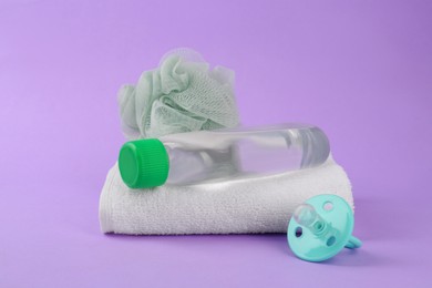 Photo of Bottle with baby oil, towel, pacifier and shower puff on violet background