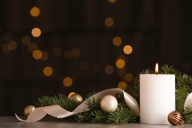 Burning white candle with Christmas decor on table against blurred lights. Space for text