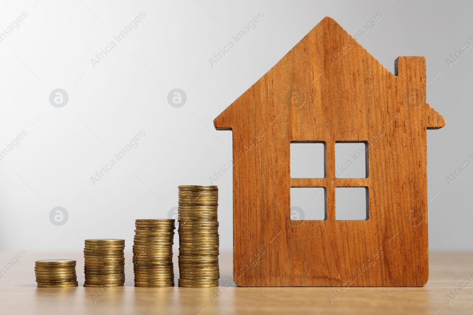 Photo of Mortgage concept. Model house and stacks of coins on wooden table against light grey background, closeup