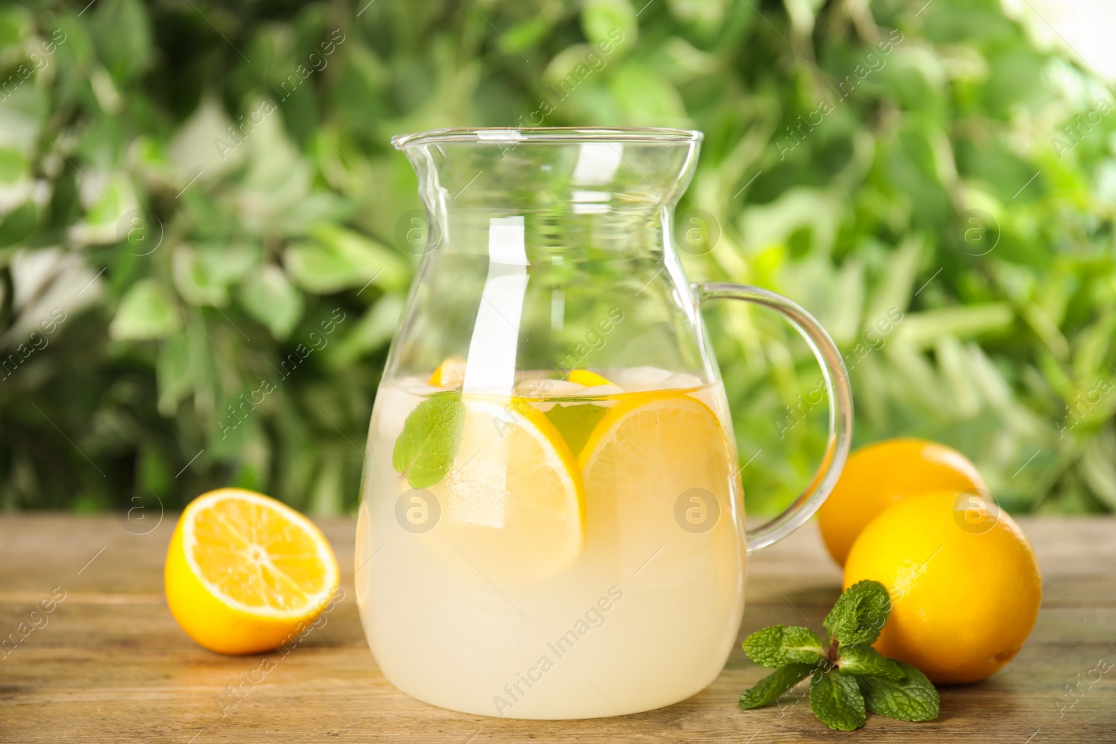 Photo of Cool freshly made lemonade in glass pitcher on wooden table