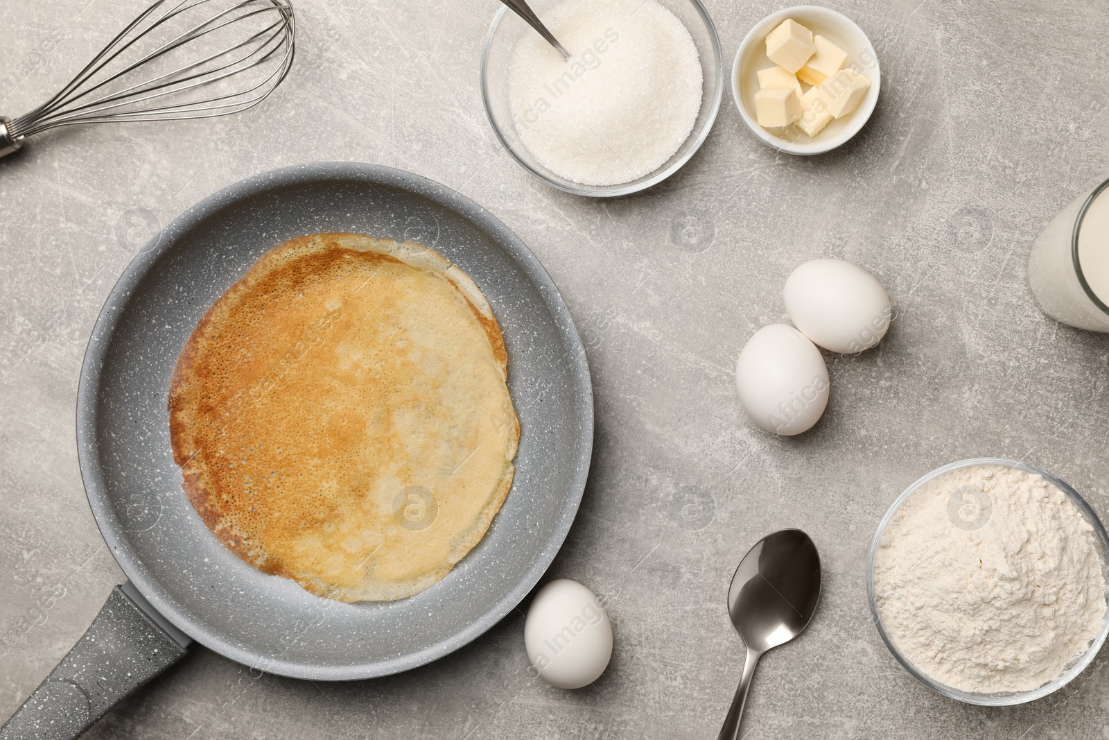 Photo of Frying pan with delicious crepe and ingredients on grey table, flat lay