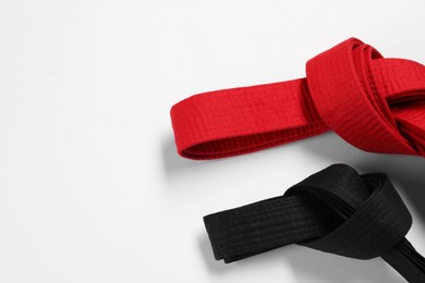 Photo of Red and black karate belts on white background, flat lay. Space for text