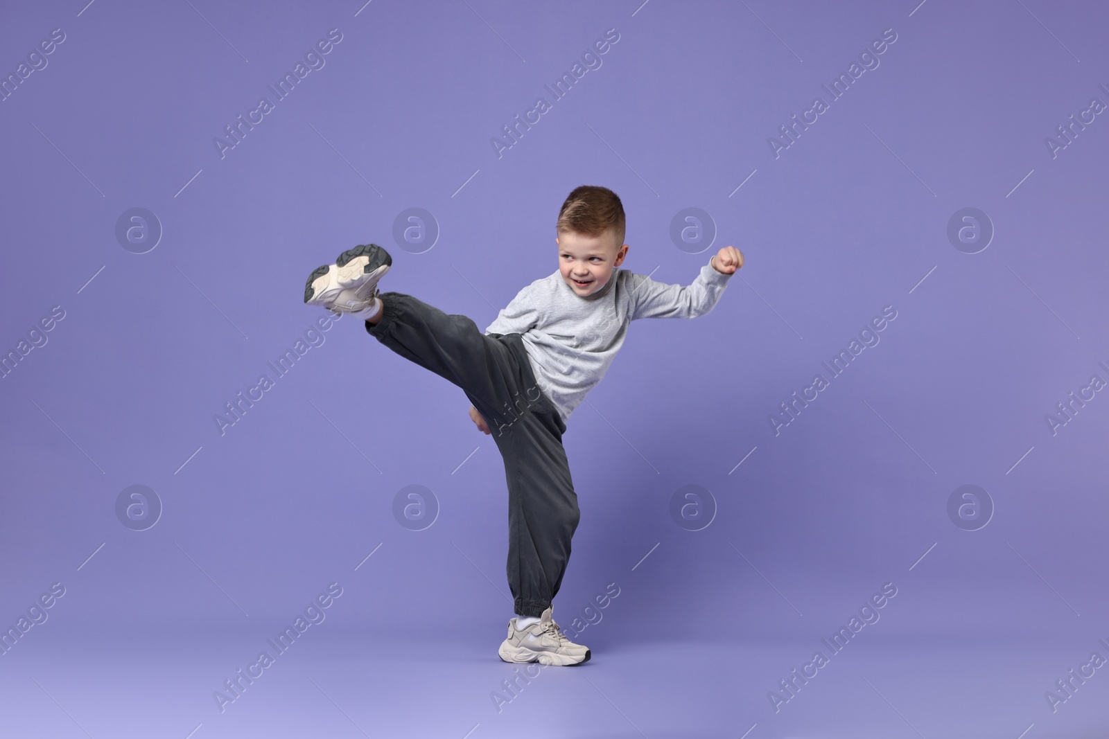 Photo of Happy little boy dancing on violet background. Space for text