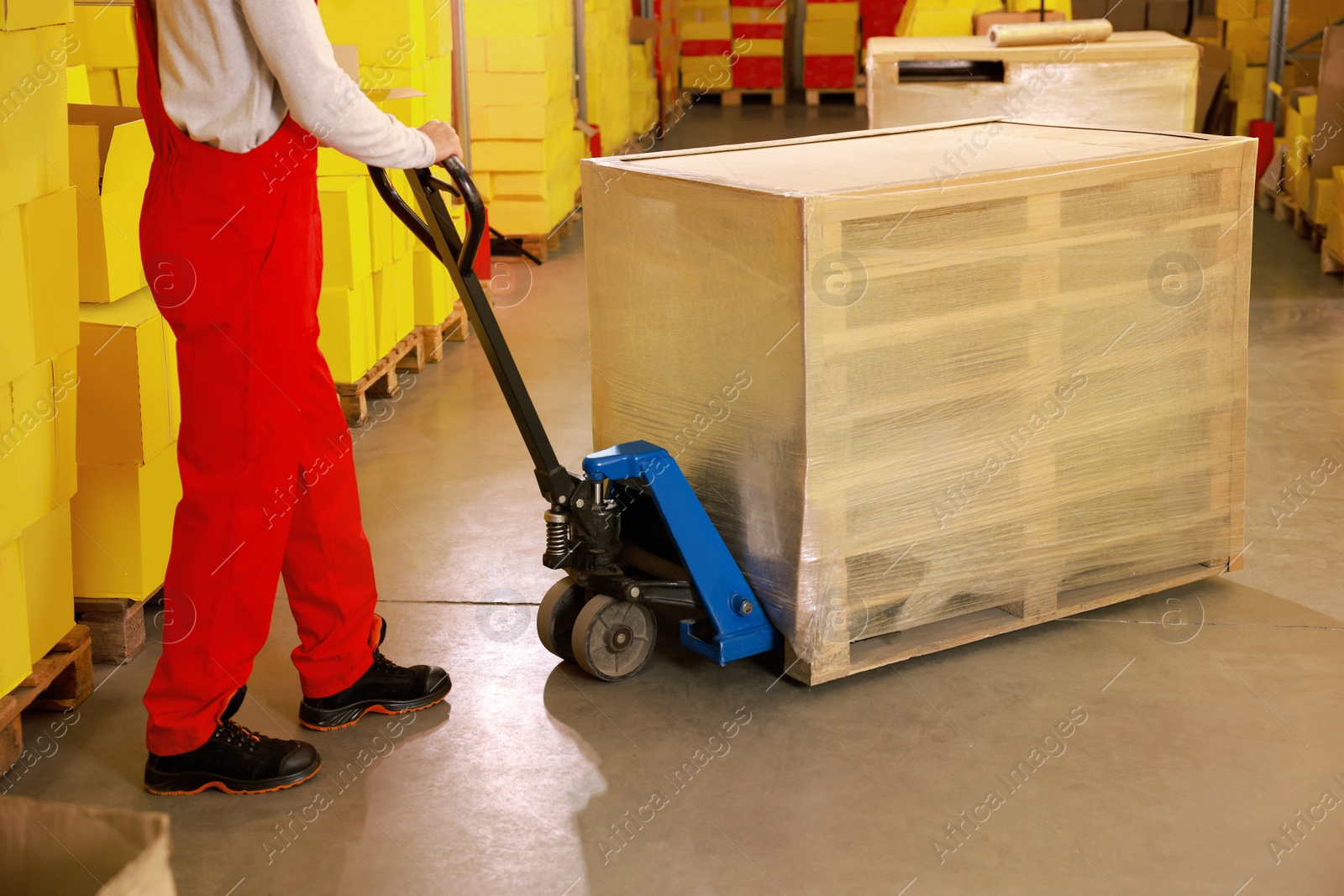 Image of Worker moving wrapped wooden pallets with manual forklift in warehouse, closeup