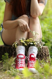 Photo of Woman sitting on stump with flowers in socks outdoors, closeup