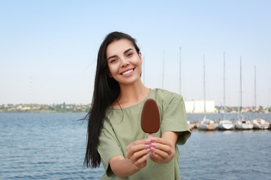 Photo of Beautiful young woman holding ice cream glazed in chocolate near river