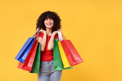 Photo of Happy young woman with shopping bags on yellow background