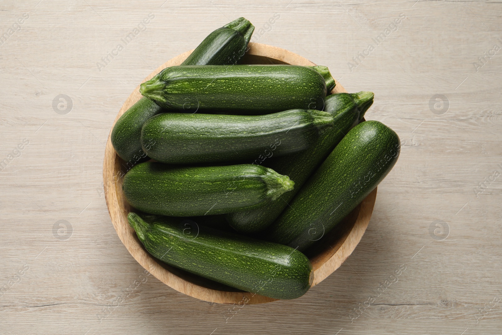 Photo of Raw ripe zucchinis in bowl on white wooden table, top view