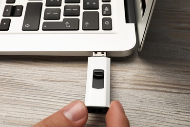 Photo of Man connecting usb flash drive to laptop at white wooden table, closeup