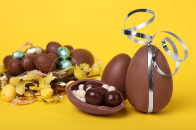 Photo of Delicious chocolate eggs and sweets on yellow background, closeup