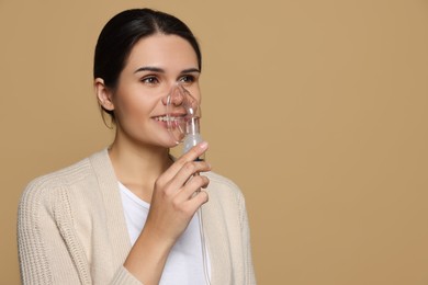 Photo of Young woman using nebulizer on dark beige background, space for text