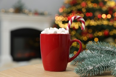 Photo of Christmas cocoa with marshmallows and candy cane in red cup on wooden table indoors, closeup