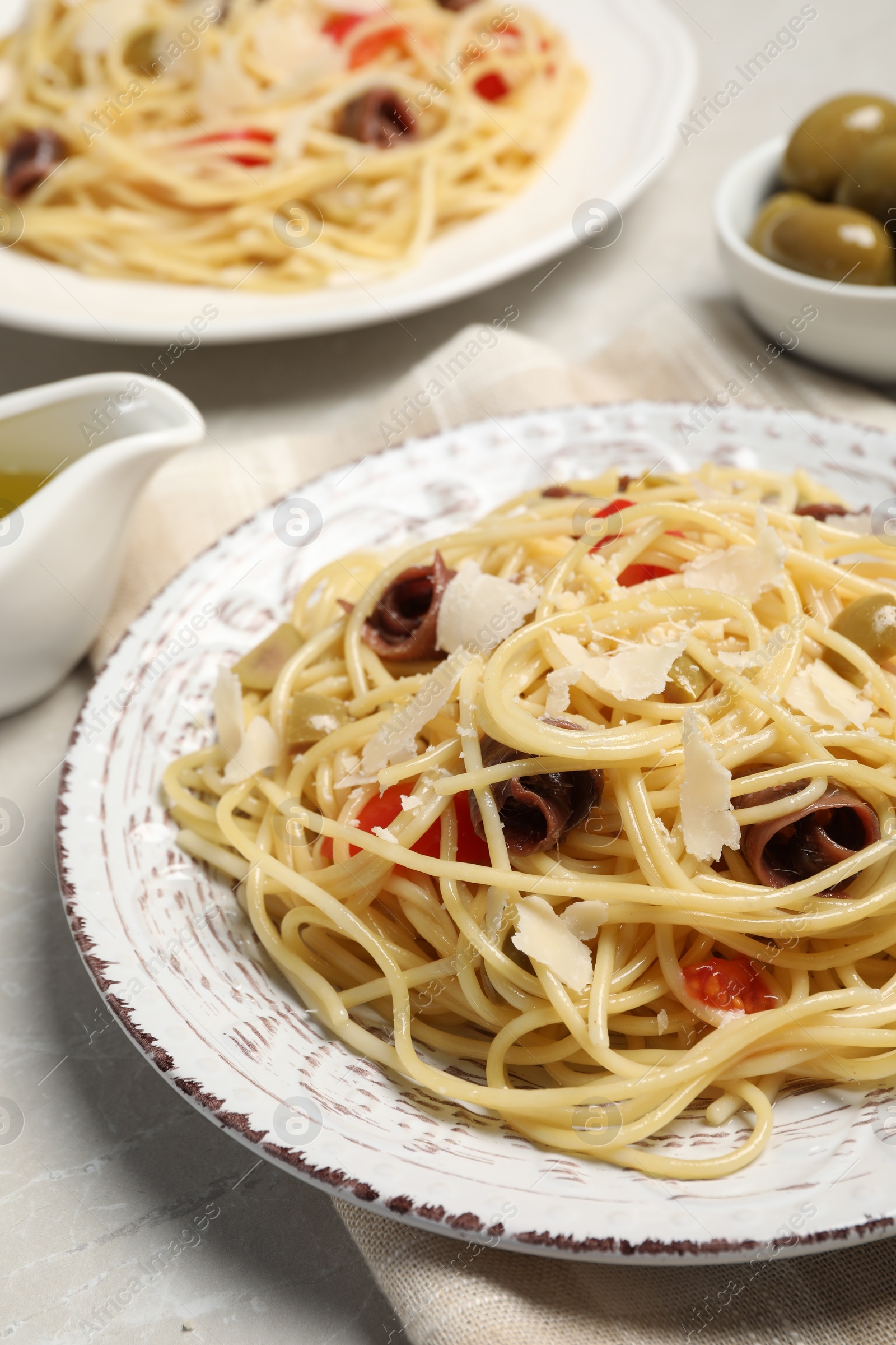 Photo of Delicious pasta with anchovies, tomatoes and parmesan cheese on light grey table