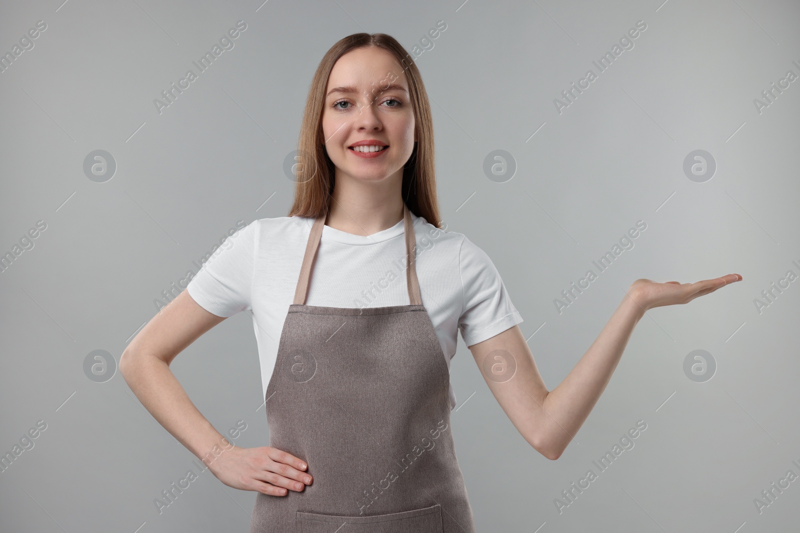 Photo of Beautiful young woman wearing kitchen apron on grey background. Mockup for design