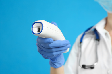 Photo of Doctor holding non contact infrared thermometer against light blue background, focus on hand. Measuring temperature