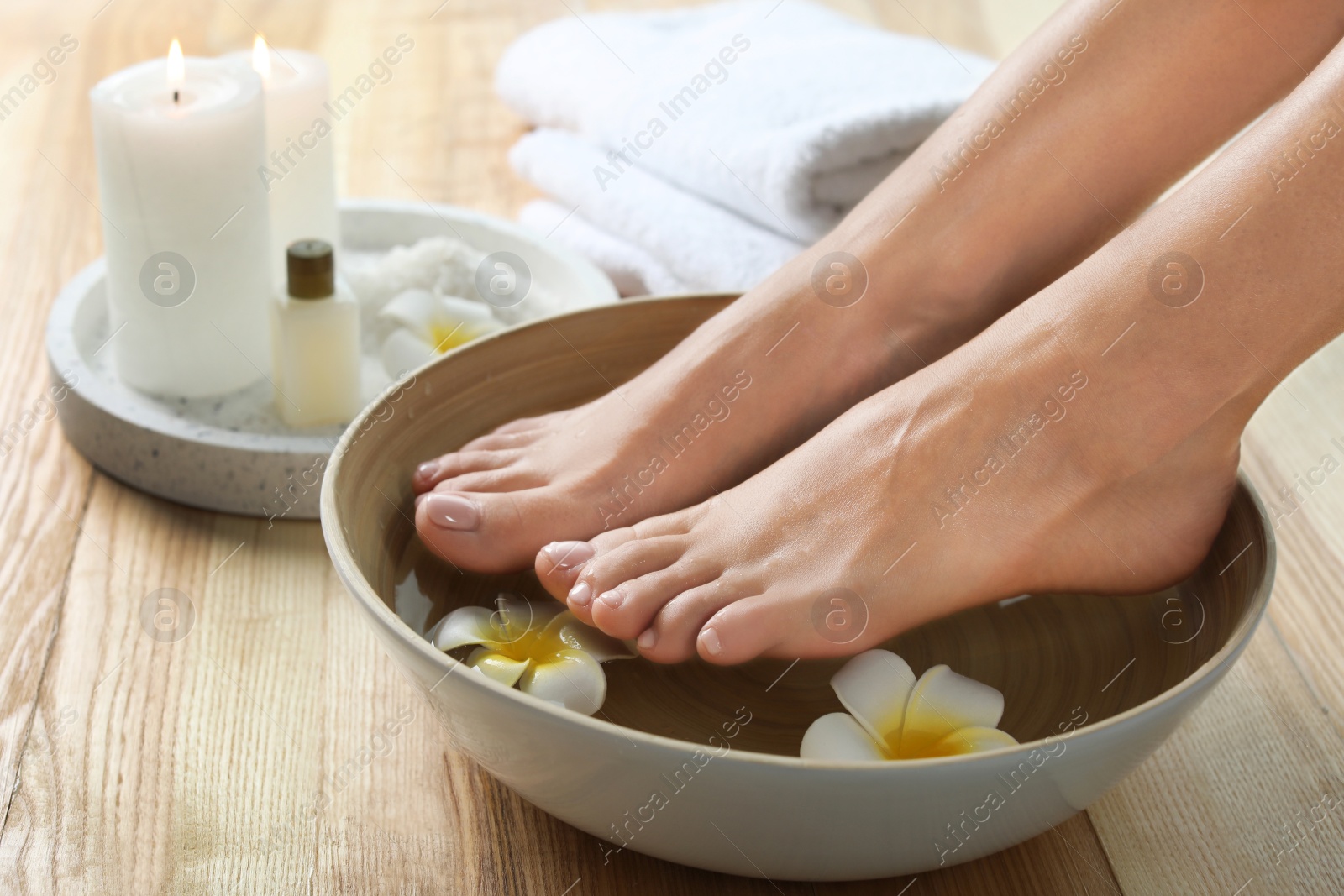 Photo of Closeup view of woman soaking her feet in dish with water and flowers on wooden floor. Spa treatment