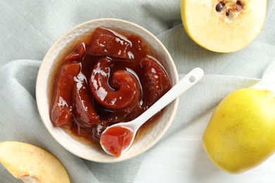 Tasty homemade quince jam in bowl, spoon and fruits on white wooden table, flat lay