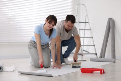 Photo of Couple applying glue onto wallpaper sheet in room