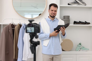 Photo of Smiling fashion blogger showing shoe while recording video at home