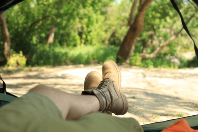 Young man resting in camping tent near forest, view from inside