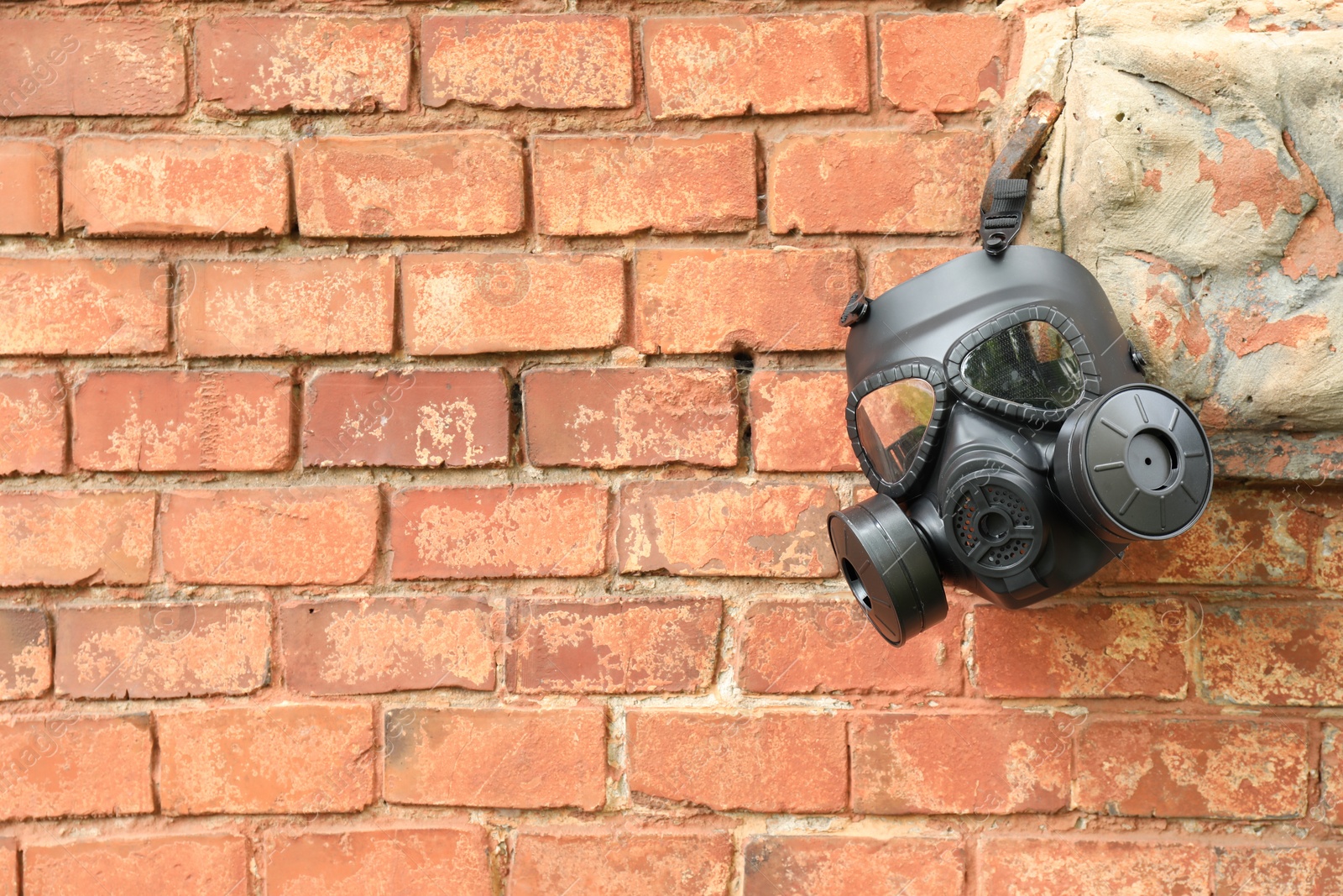 Photo of One gas mask hanging near brick wall on building. Space for text