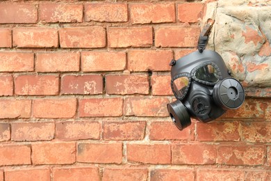 Photo of One gas mask hanging near brick wall on building. Space for text