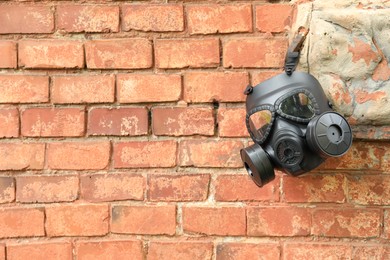 One gas mask hanging near brick wall on building. Space for text