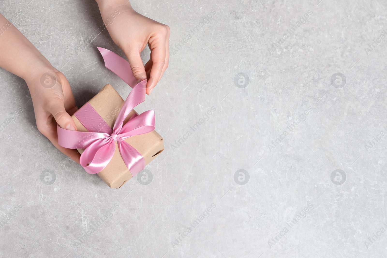 Photo of Woman holding gift box with pink bow at light grey table, top view. Space for text