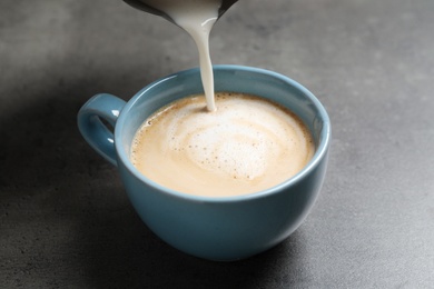 Photo of Pouring milk into cup of coffee on grey table, closeup