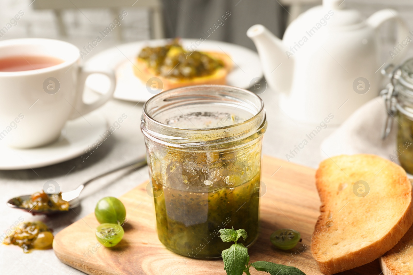 Photo of Jar of delicious gooseberry jam, toasts and fresh berries on table