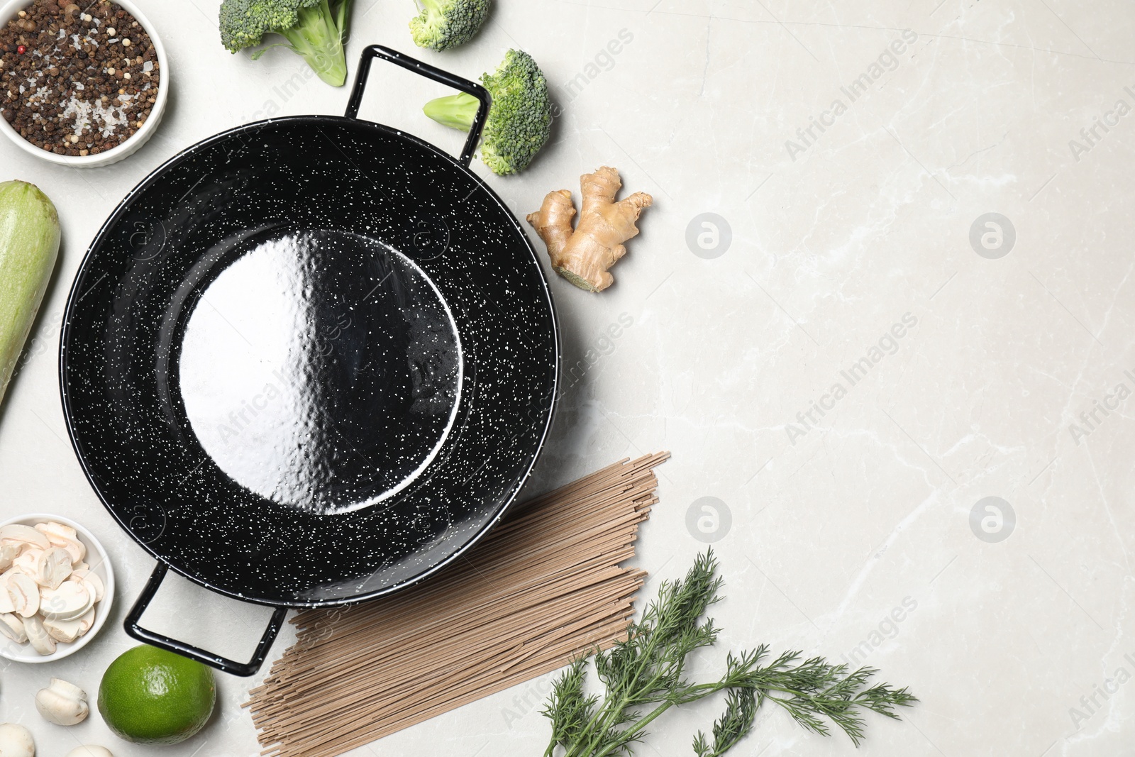 Photo of Empty iron wok surrounded by raw ingredients on light table, flat lay. Space for text